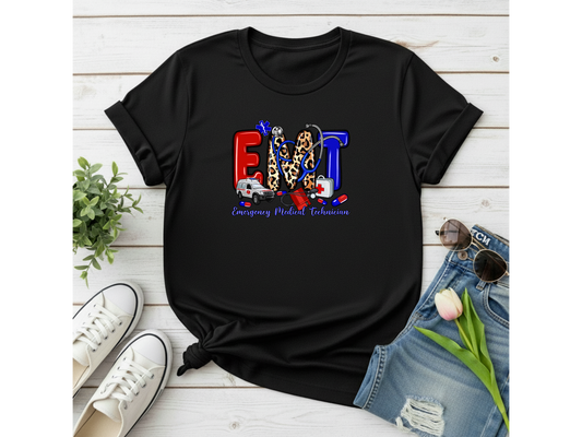 Black t-shirt with colorful 'EMT' design on a wooden surface with shoes and jeans.