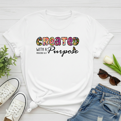 White t-shirt with 'Created with a Purpose' text on a wooden surface with shoes, jeans, and sunglasses.