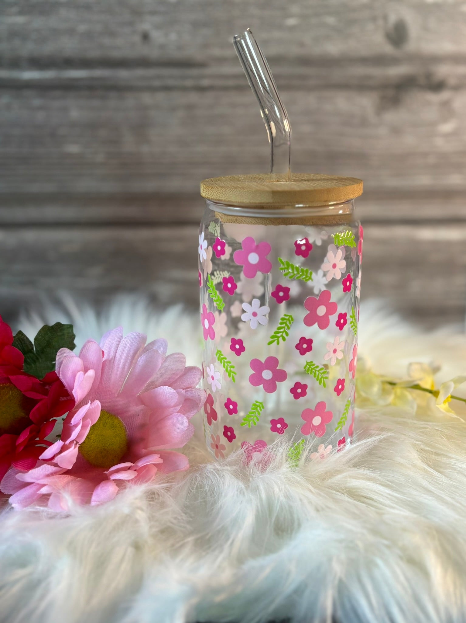 Glass tumbler with floral design and wooden lid on a fluffy white surface with flowers.