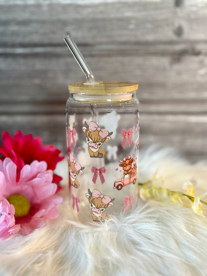 Clear tumbler with cartoon designs and a straw lid, surrounded by flowers on a soft surface.